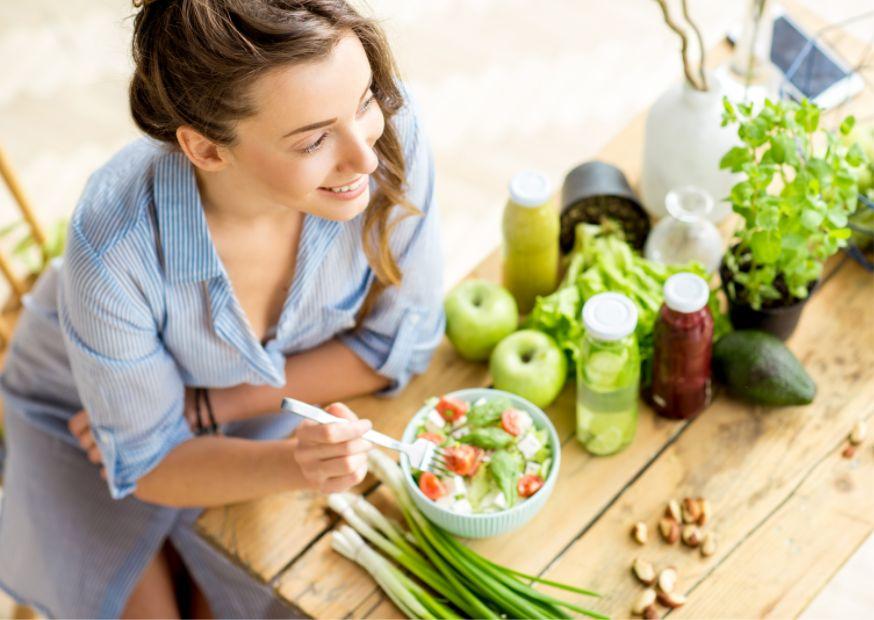 frau isst salat obst und gemüse auf dem tisch